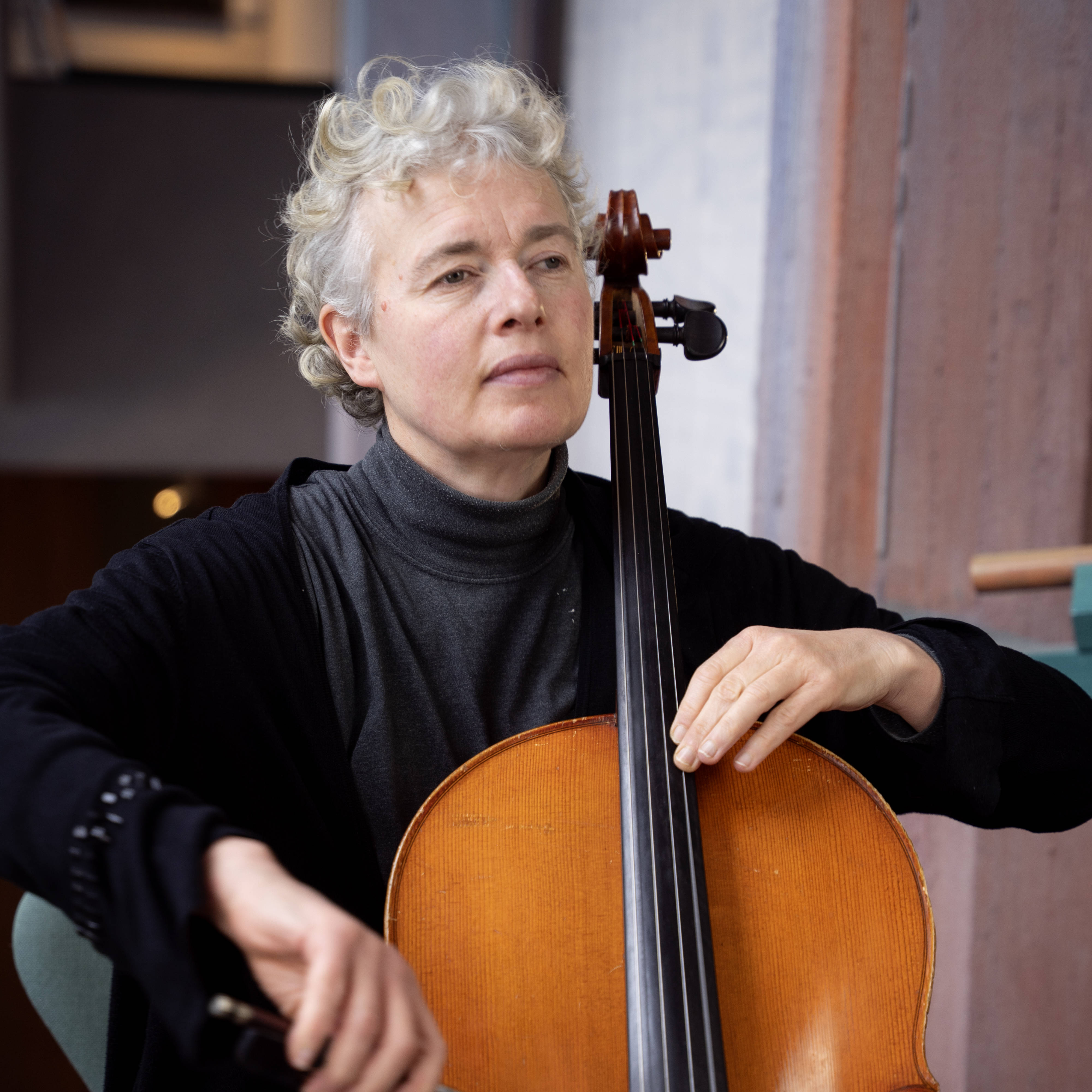 Fotogrfie einer Frau, die Cello spielt. Sie trägt schwarze Kleidung, hat kurzes, lockiges Haar und helle Haut.
