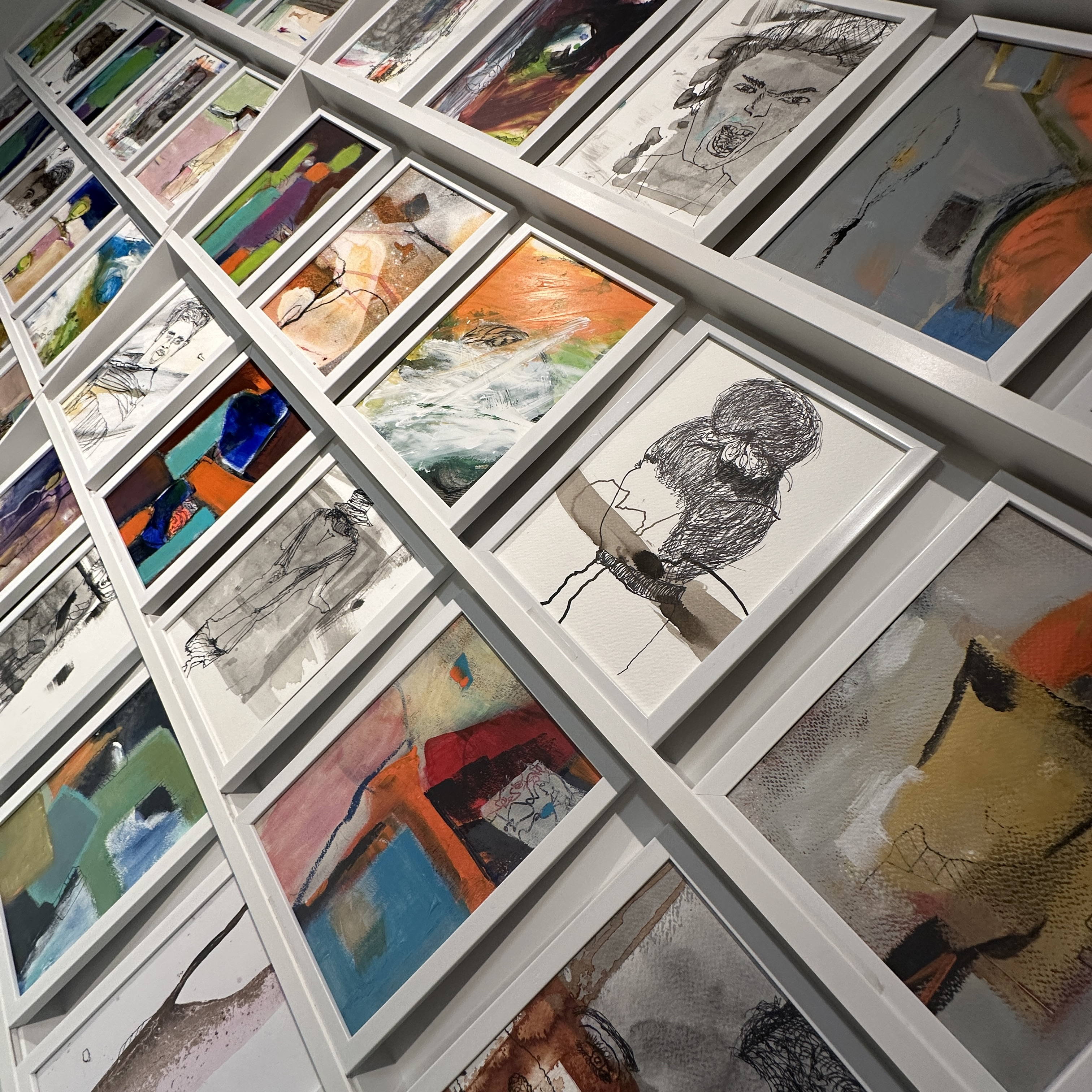 Fotografie einer Wand, die mit kleinformatigen Malerei-Werken behangen ist. Zu sehen sind unterschiedliche Motive, mal farbig, mal schwarz-weiß-Zeichnungen. Sie stammen von der Künstlerin Maike Remane.